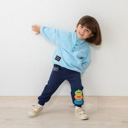 水色のフリースと紺色のスウェットパンツを着用した幼い女の子が笑顔でポーズをとっています。