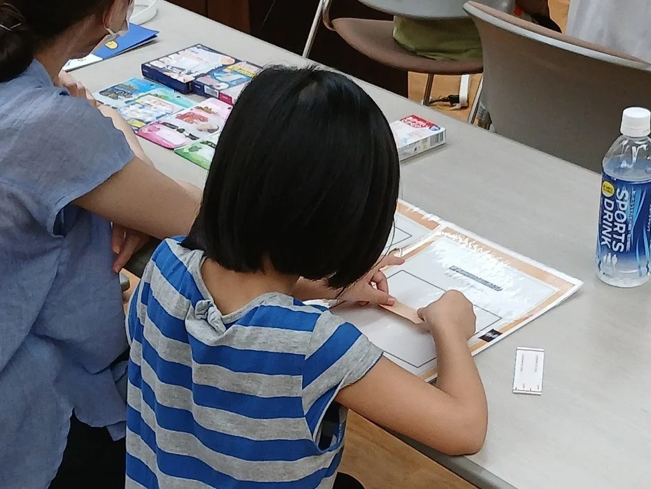 子供と大人が机に向かい紙を使った作業に集中している様子