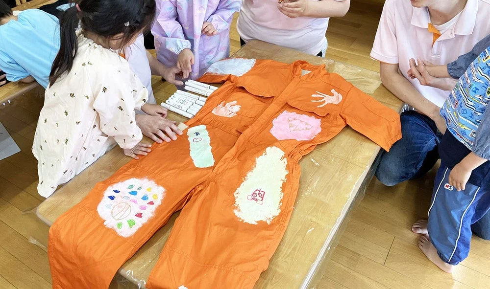 子供たちがオレンジ色のつなぎに絵を描き装飾している様子