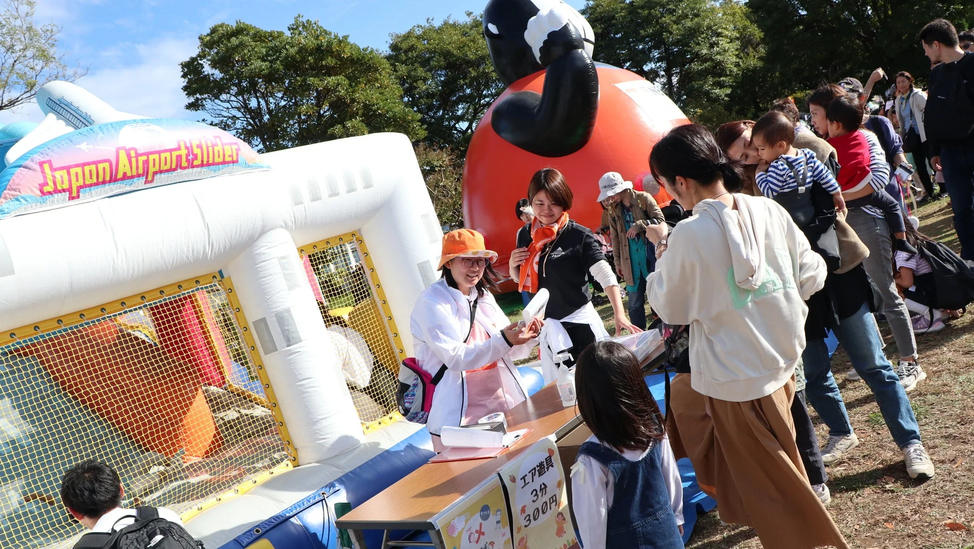 屋外イベントで、多くの家族連れや子供たちが賑わっている。巨大なエア遊具「Japan Airport Slider」があり、係員が受付で対応している。