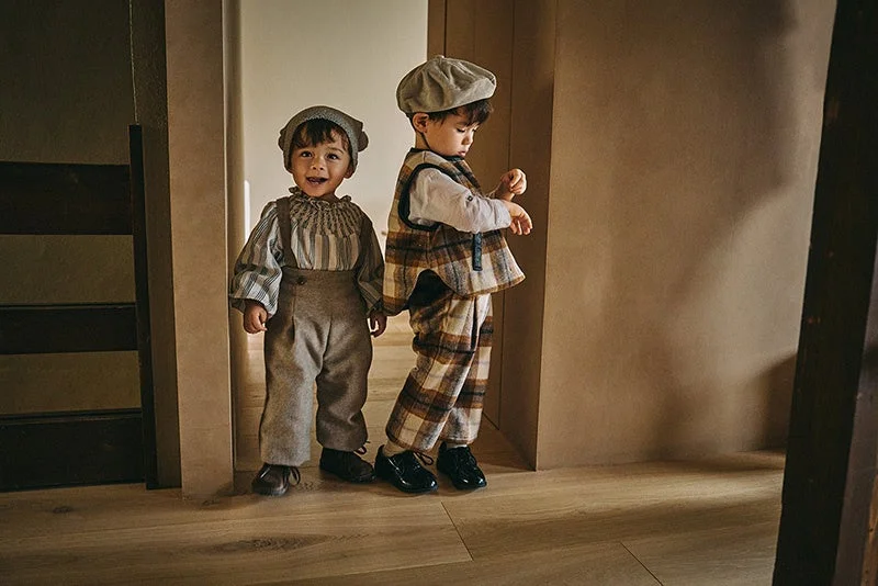 おしゃれな帽子と洋服を着た幼い二人の子供が室内に立っています。