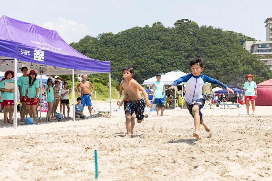 晴れた夏のビーチで、ライフセービングクラブのイベントに参加する子供たちが砂浜を力強く走っている様子