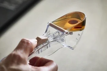 透明な計量スプーンに琥珀色の液体が入っており、それを手が持っているクローズアップ画像