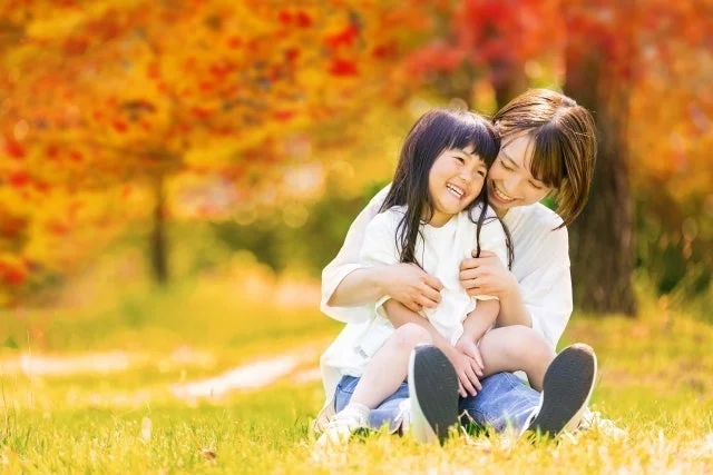 紅葉した木々を背景に、母親が子供を抱きしめ、二人で楽しそうに笑っている