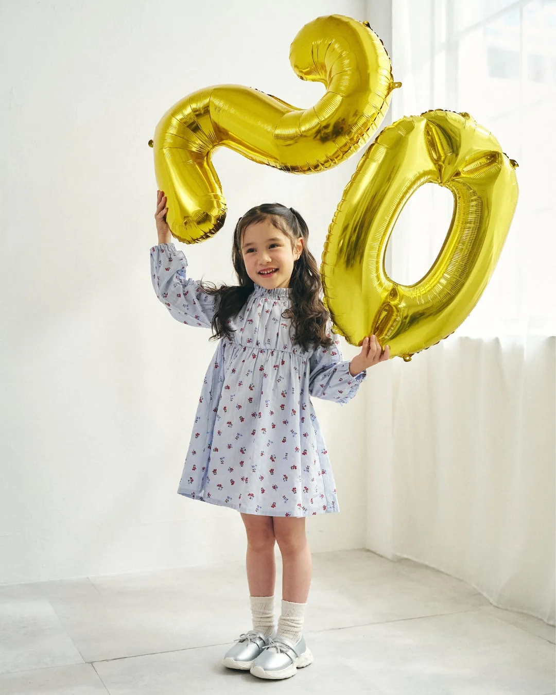 水色の花柄ドレスを着て「20」バルーンを持つ女の子