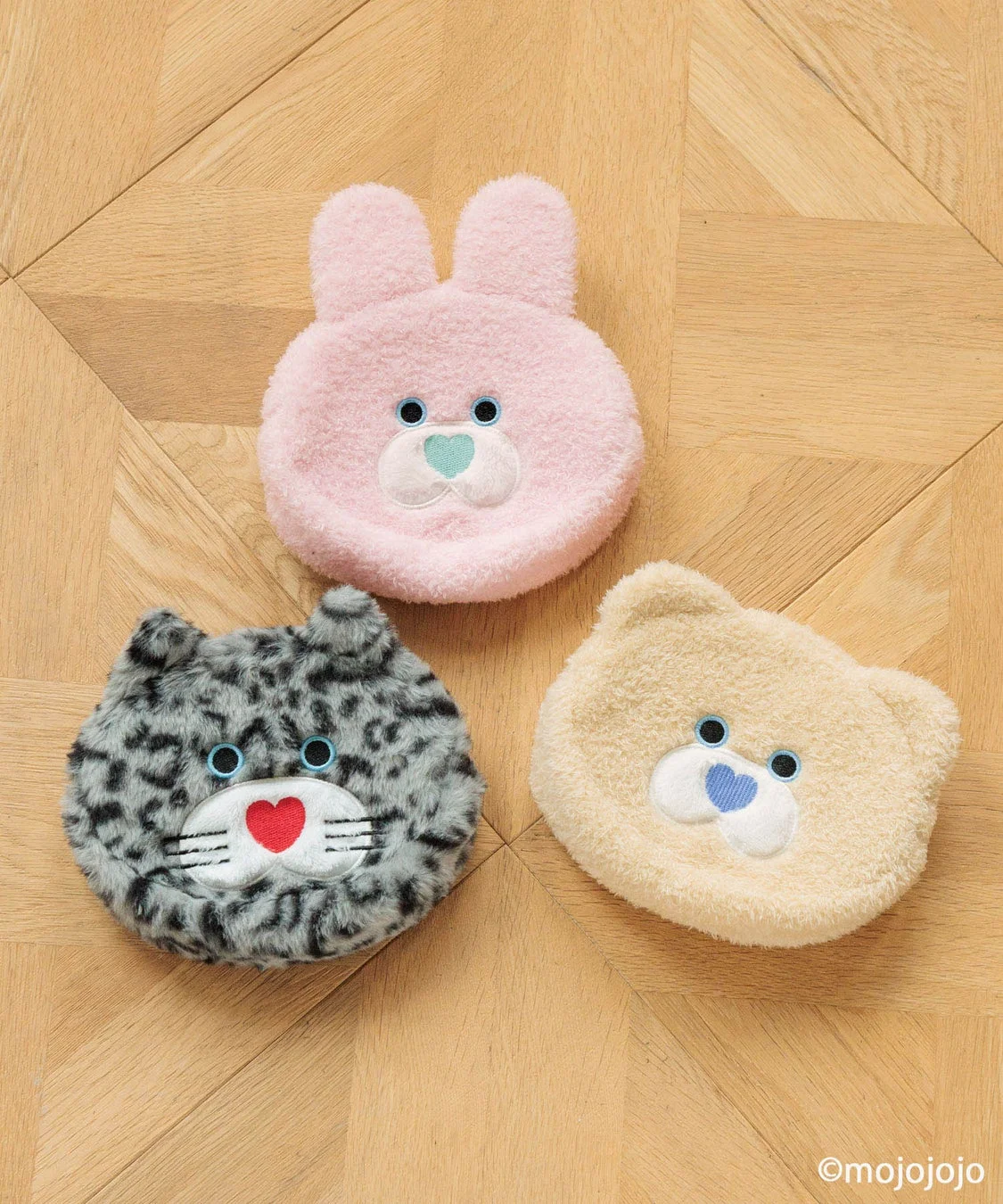 木の床に置かれた、うさぎ、ネコ、クマの形をした可愛らしいふわふわのポーチ3点。それぞれピンク、グレー、クリーム色で、ハートの鼻と刺繍の顔が特徴的です。